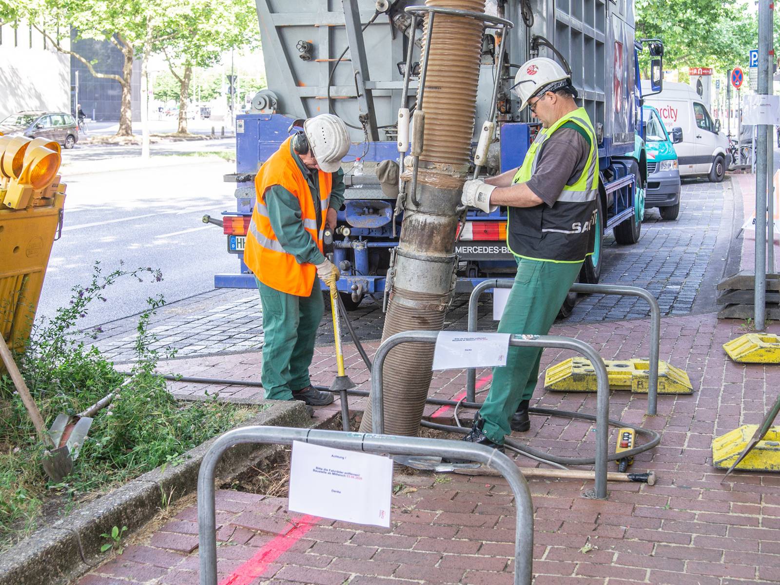 Zwei Männer mit einem Sauger, der ins Erdreich führt. 