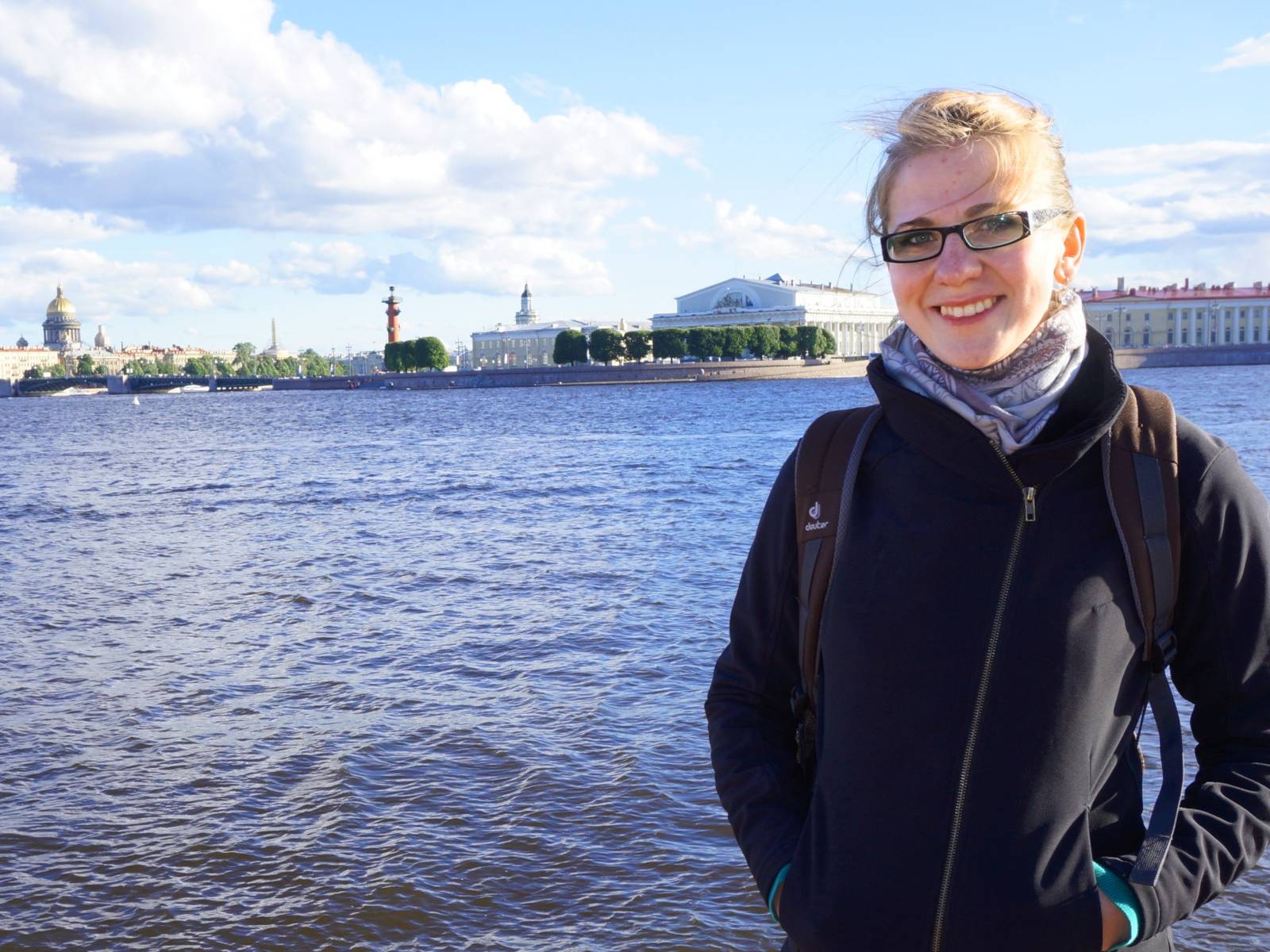 Frau vor einem Gewässer. Im Hintergrund eine am Fluss liegende Stadt.