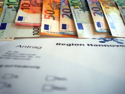Geldscheine hängen nebeneinander, darunter ist ein Antragsformular der Region Hannover für Fördergeld.
