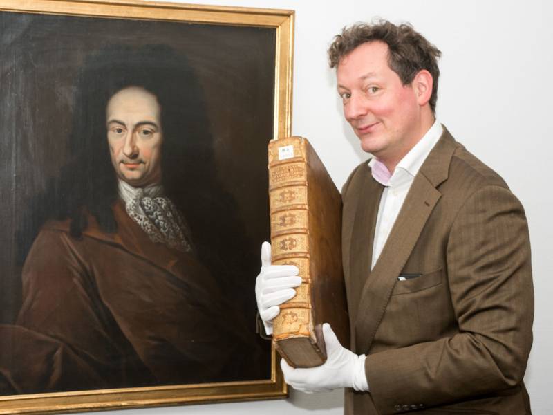 Mann mit voluminösen, alten Bild im Arm vor einem historischen Gemälde