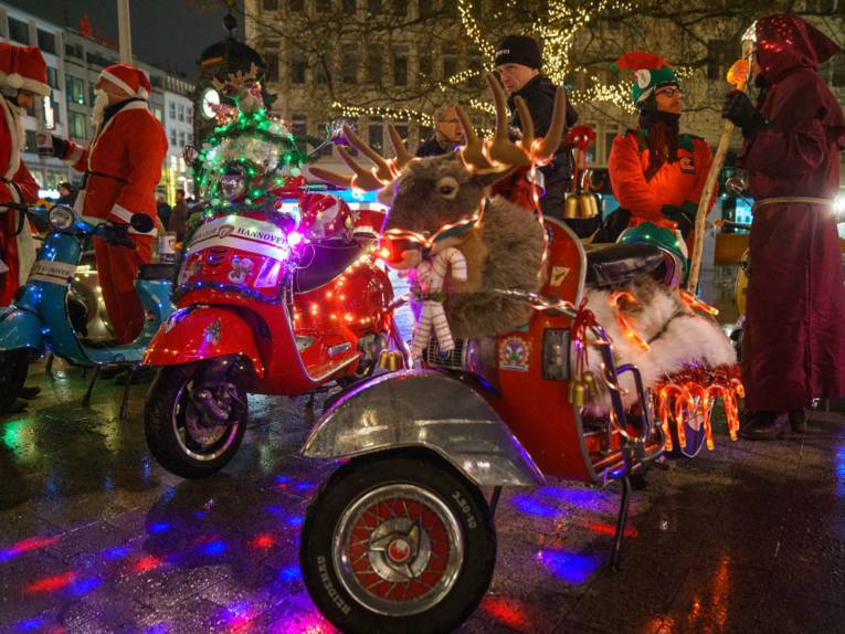 Weihnachtliche geschmückte Motorroller und als Weihnachtsmänner oder Wichtel verkleidete Menschen am Kröpcke