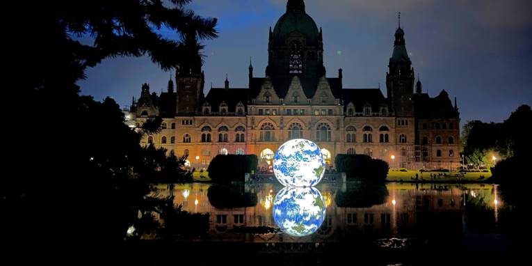 Beleuchtete schwimmende Weltkugel auf dem Maschteich abends, im Hintergrund das Neue Rathaus