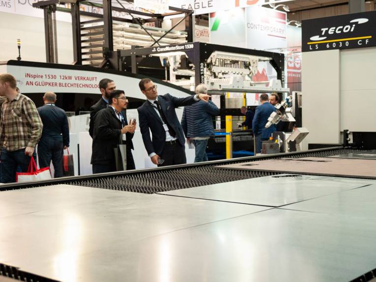 Ein Mann erklärt anderen Männer etwas vor einer großen Maschine mit Metallplatten.