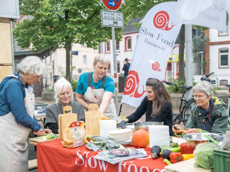 Fünf Frauen sitzen an einem Tisch und schneiden Gemüse.