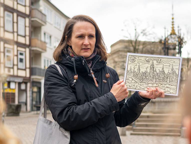 Karo Quambusch M.A. während einer Führung auf dem Holzmarkt mit der Tafel einer Stadtansicht in der Hand, Digitalfoto, März 2024, Ulrich Pucknat