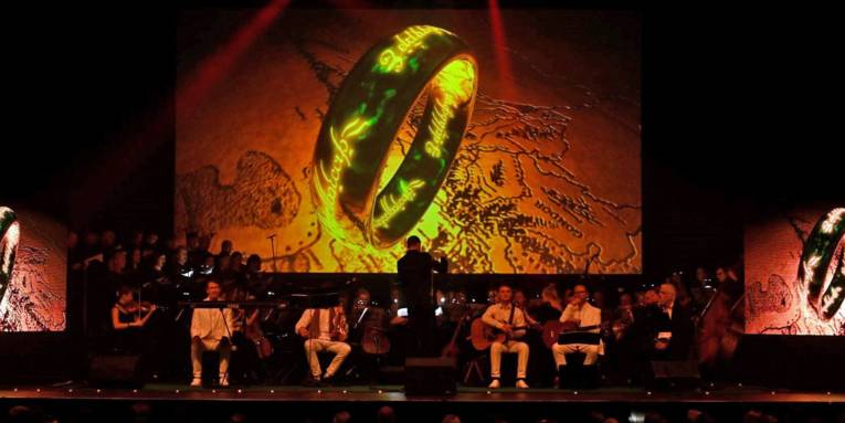 Das Orchester sitzt vor einer großen Leinwand mit einem Ring darauf.