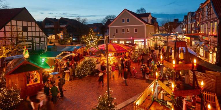 Menschen und weihnachtliche Buden auf einem Dorfplatz.