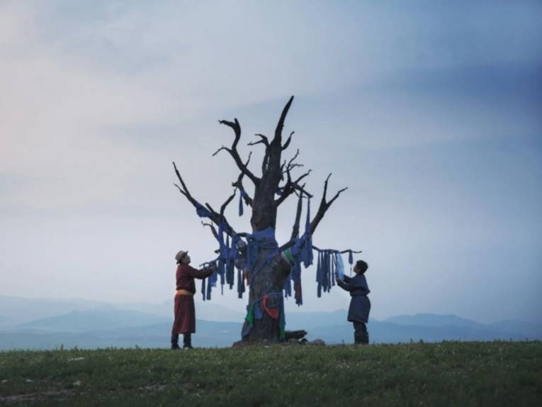 Ein Mann und ein Junge hängen Tücher an die verdorrten Äste eines Baumes.